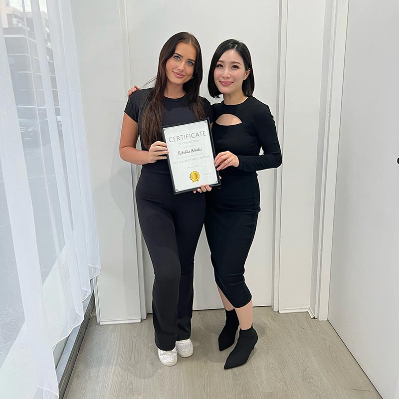Bek holding up certification after graduating eyeliner tattoo course with a tattoo master